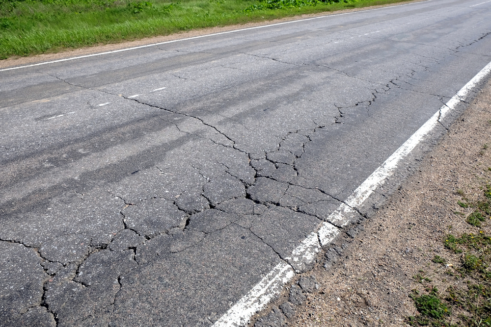 A close-up of a rutted and cracked asphalt surface on a hot summer day
