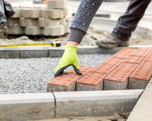 Construction,Worker,Placing,Red,Concrete,Paving,Stones,In,Gravel,Bed